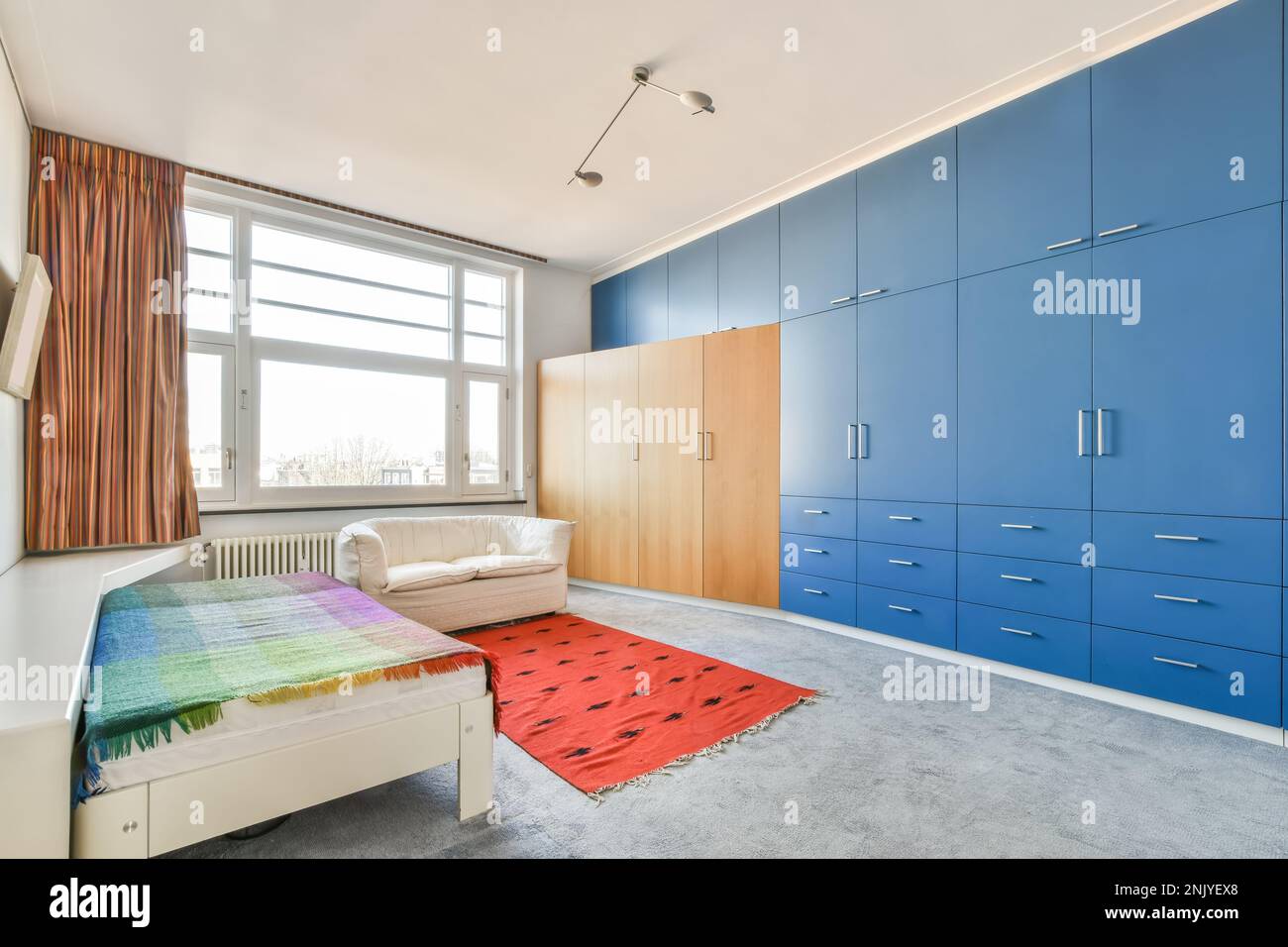 Innendesign des geräumigen Schlafzimmers mit Teppichboden und rotem Teppich in der Nähe des Einzelbetts Stockfoto