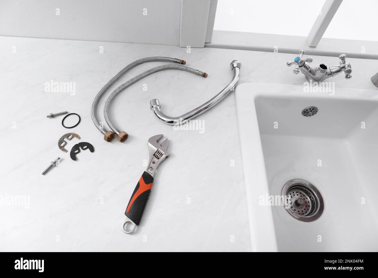 Teile des Wasserhahns und Schraubenschlüssels auf der Arbeitsfläche aus weißem Marmor in der Küche Stockfoto