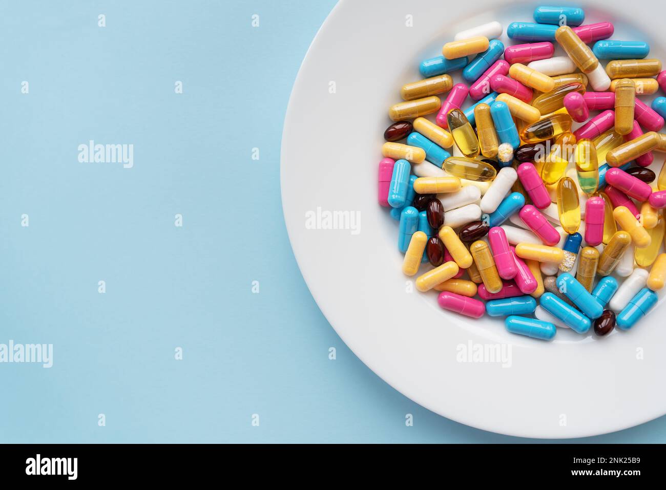 Bunte Pillen in einer großen weißen Schüssel auf blauem Hintergrund. Gesundheitsbegriff und evidenzbasierte Medizin Stockfoto