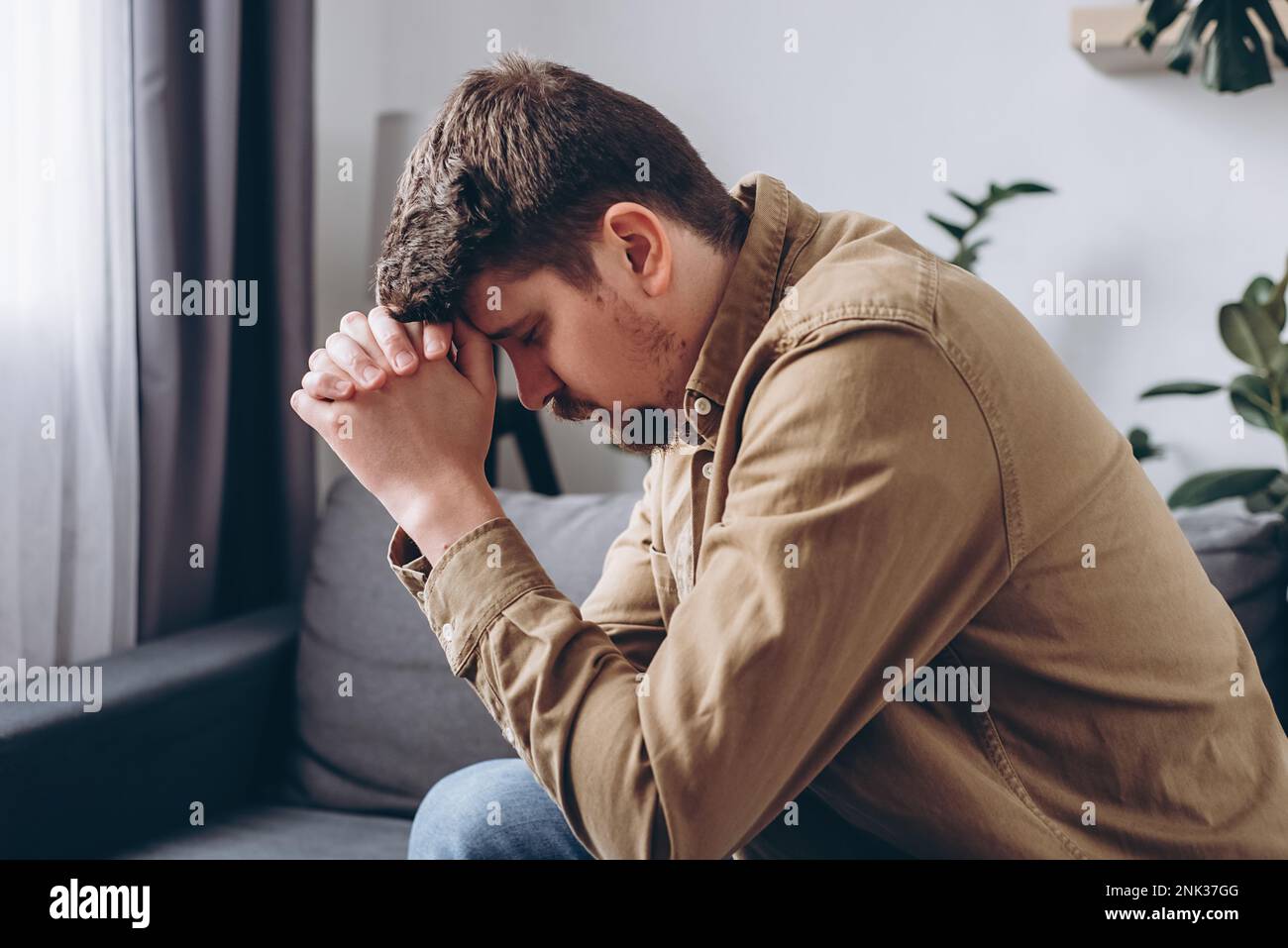 Nahaufnahme eines stressigen, traurigen jungen Mannes, der allein auf dem Sofa im Wohnzimmer sitzt und sein Gesicht mit Händen bedeckt. Depression männlicher 30s-Jähriger, verärgert und unh Stockfoto