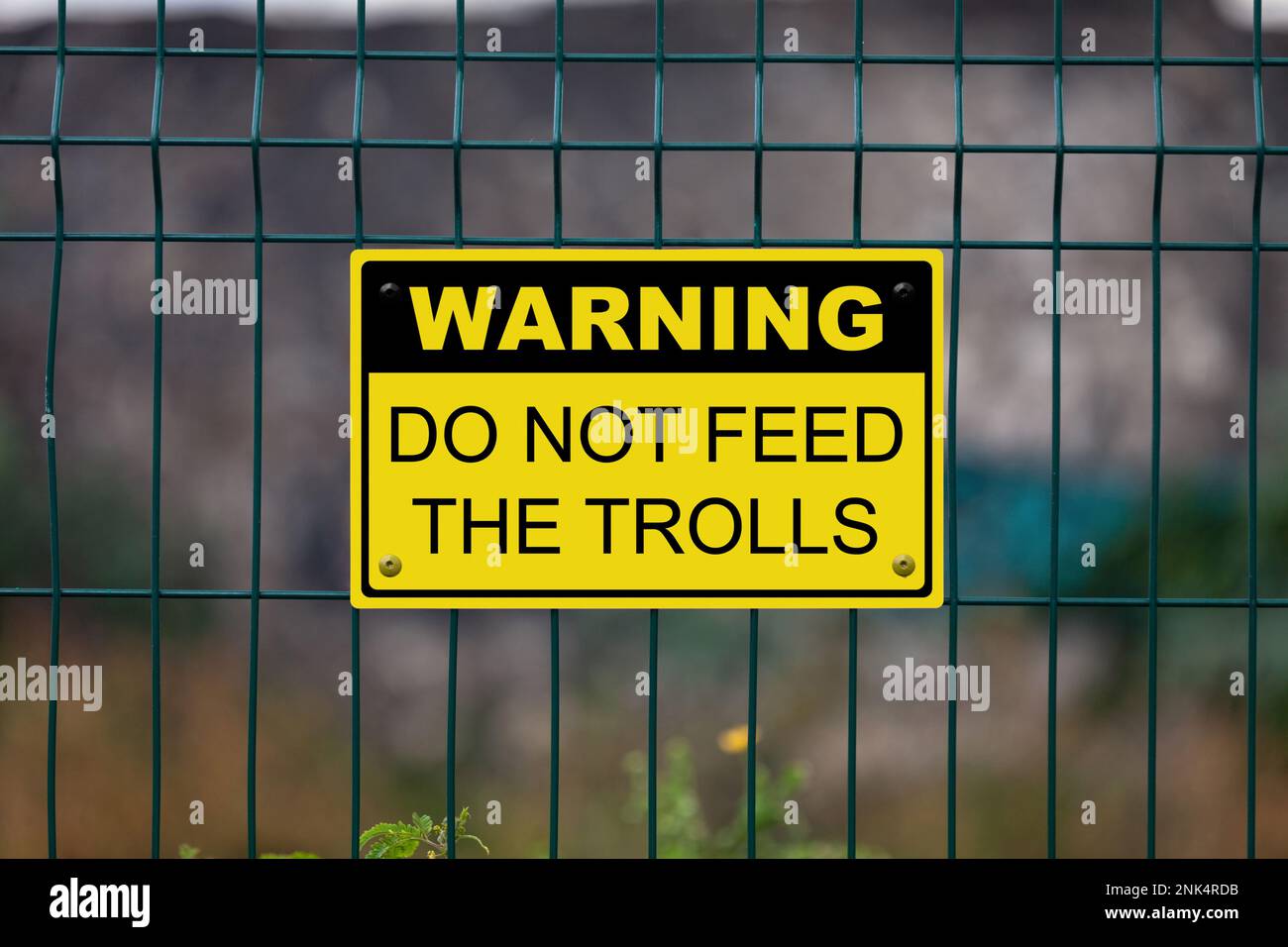 Schwarzes und gelbes Warnschild an einem Zaun. Das Schild mit der Aufschrift „Warnung - füttern Sie die Trolle nicht“. Stockfoto