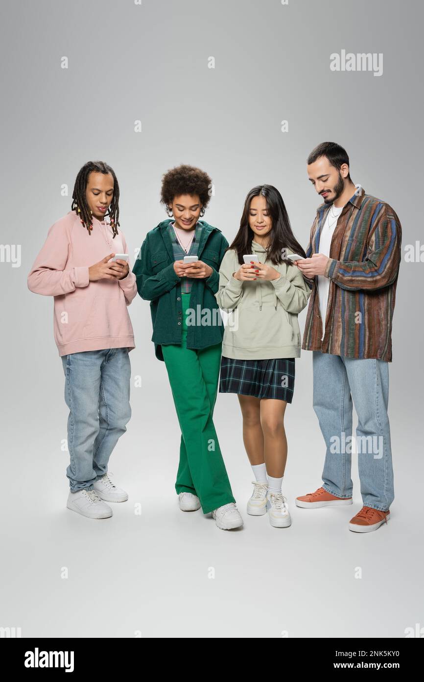 Volle Länge der Nachrichten von trendigen, multiethnischen Freunden auf Mobiltelefonen auf grauem Hintergrund, Aktienbild Stockfoto