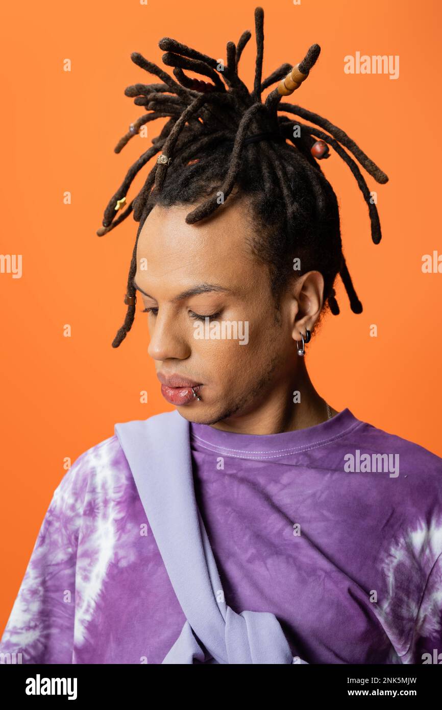 Porträt eines multiethnischen Mannes mit Dreadlocks und Piercing isoliert auf orangefarbenem Stockbild Stockfoto