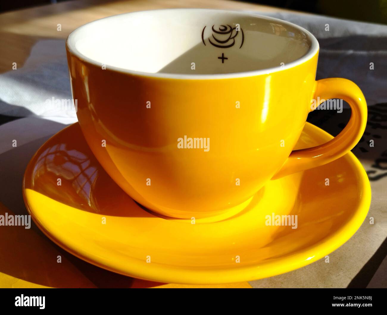 Leere Cappuccino-Tasse oder -Tasse aus gelbem Porzellan in der Nahaufnahme. Glänzende, reflektierende, glatte Oberfläche. Starke Schatten. Konzept des Kaffeeverbrauchs. Stockfoto