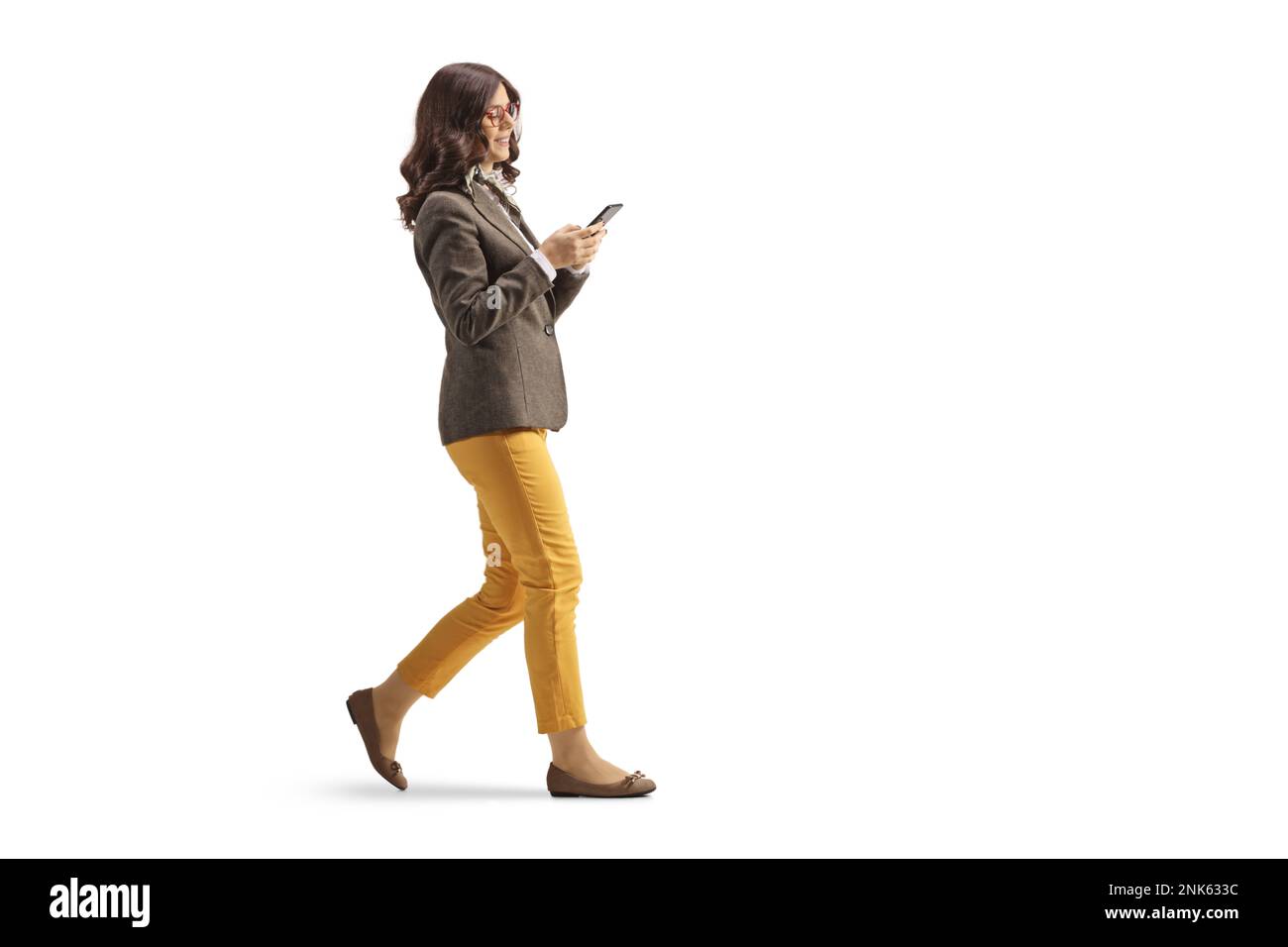 Profilaufnahme über die gesamte Länge einer jungen Frau in formeller Kleidung beim Gehen mit einem Smartphone, isoliert auf weißem Hintergrund Stockfoto