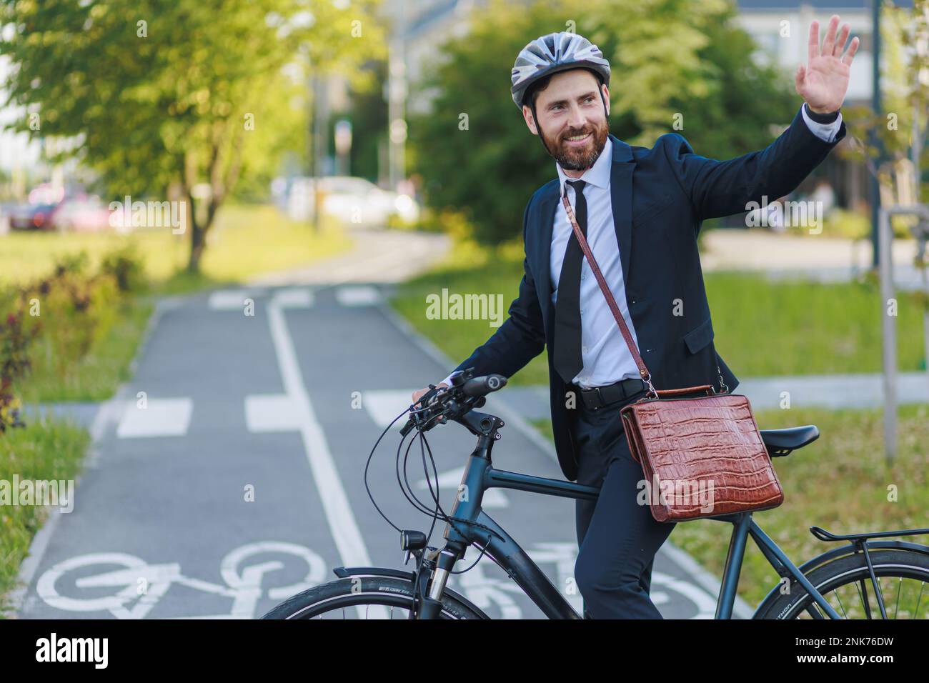 Lächelnder männlicher Manager sagte Auf Wiedersehen nach der Arbeit, während er auf der Straße Fahrrad fuhr. Seitenansicht eines glücklichen Chefs in formeller Kleidung, der auf dem Radweg steht und Stockfoto