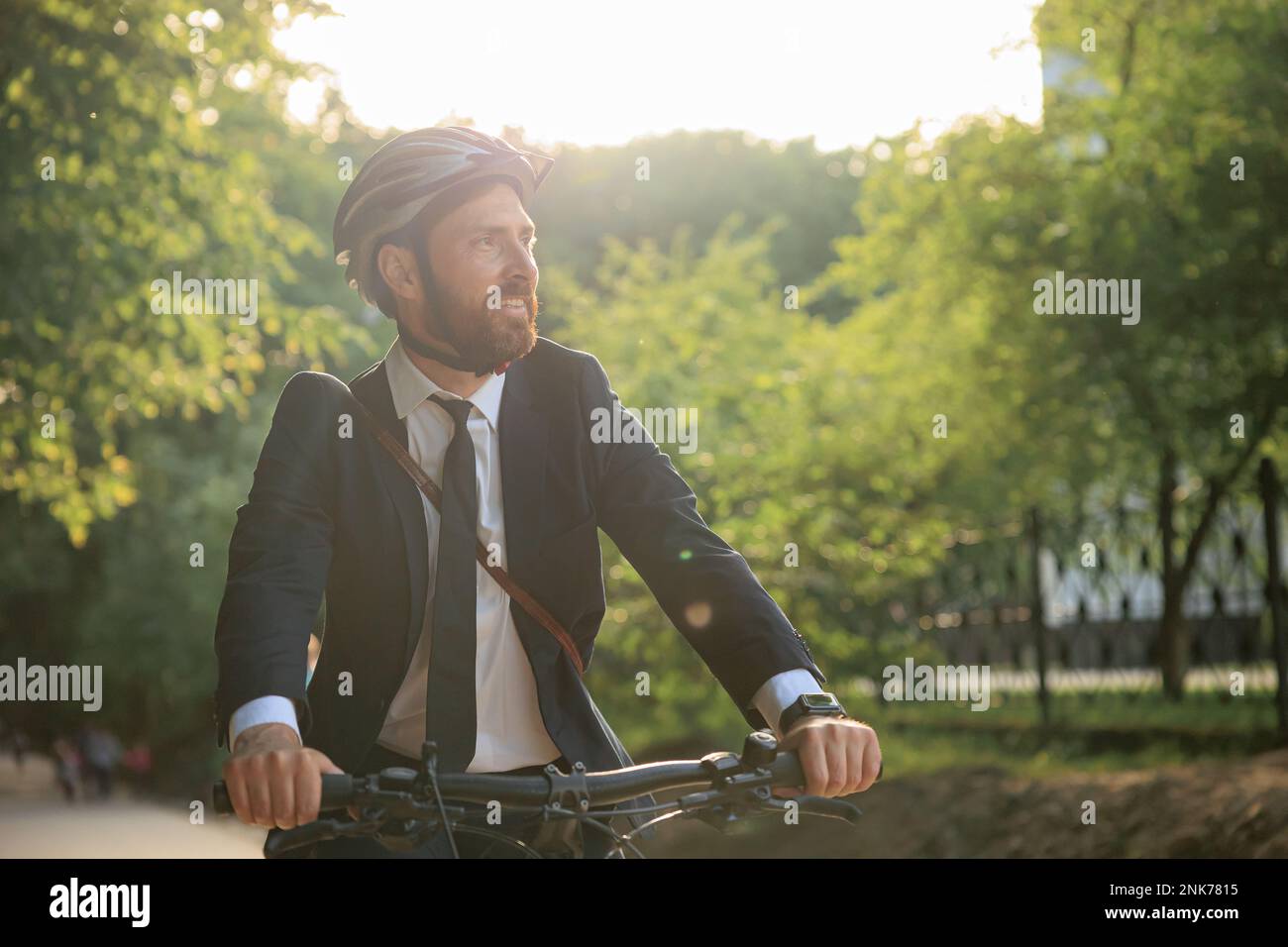 Geschäftsreisende, die bei glänzendem Wetter mit dem Fahrrad in der Stadt unterwegs sind. Porträt eines lächelnden weißen Mannes im Anzug, der den Lenker hält und etwas in Betracht zieht Stockfoto