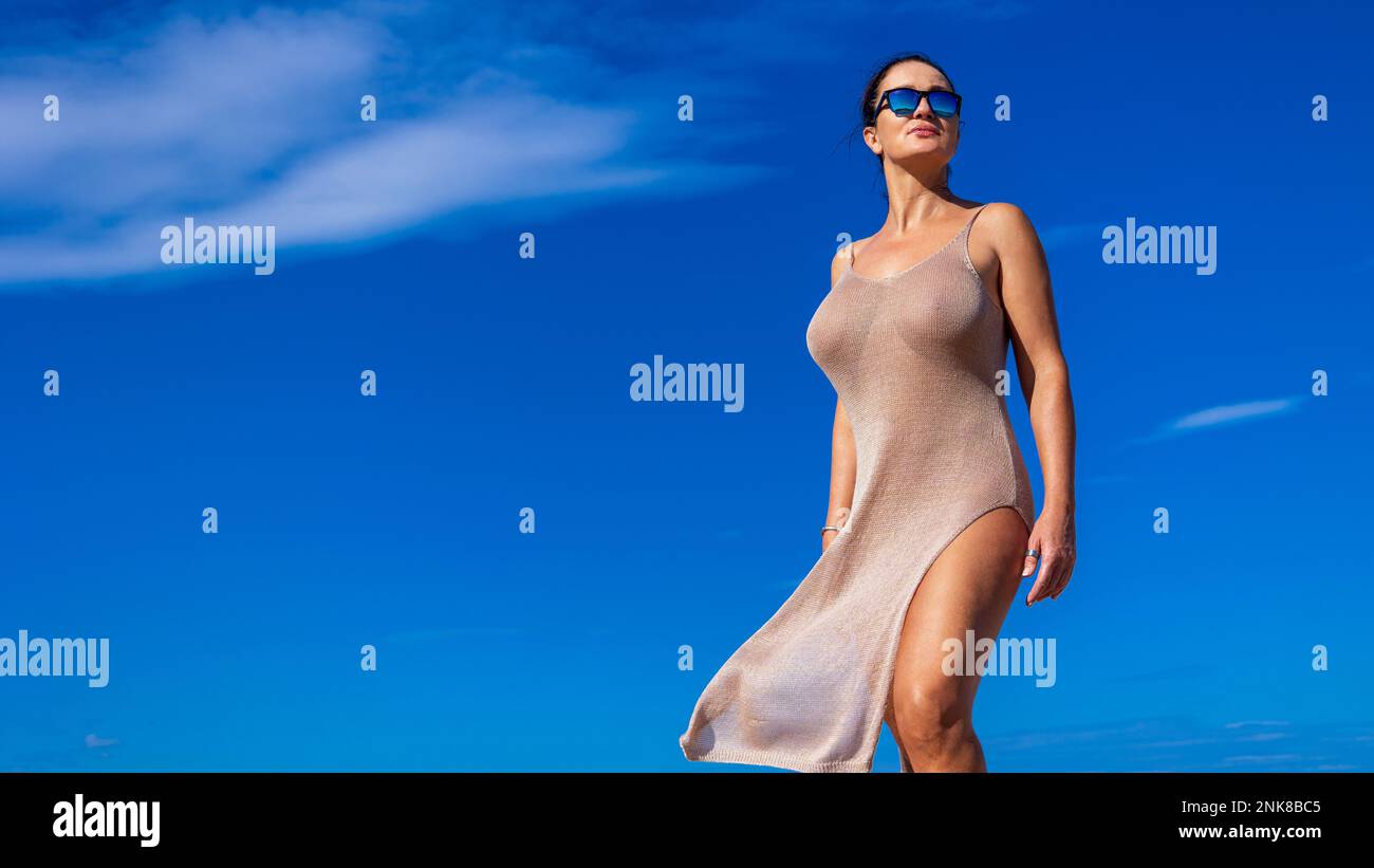 Eine Frau mit Sonnenbrille steht am Strand gegen den Himmel im Licht der untergehenden Sonne. Costa Brava, Spanien, ist ein beliebtes Urlaubsziel. Stockfoto