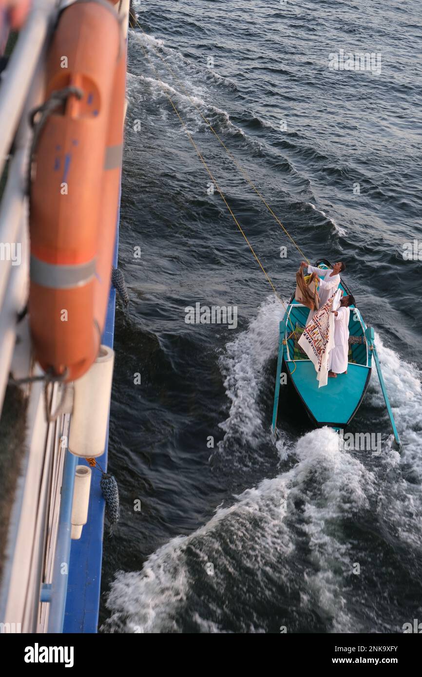 Männer, die Touristenschmuck und Textilgeschenke von einem kleinen Boot aus verkaufen, das an ein Kreuzfahrtschiff auf dem Nil gebunden ist Stockfoto
