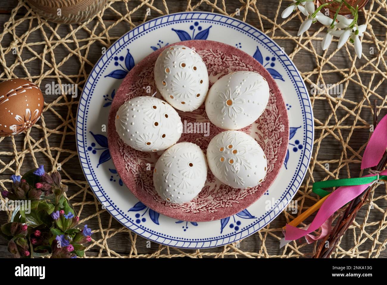Weißes Osterei mit Wachs und Frühlingsblumen dekoriert - Schneetropfen und Lungenkraut, mit tschechischer Peitsche namens Pomlazka Stockfoto