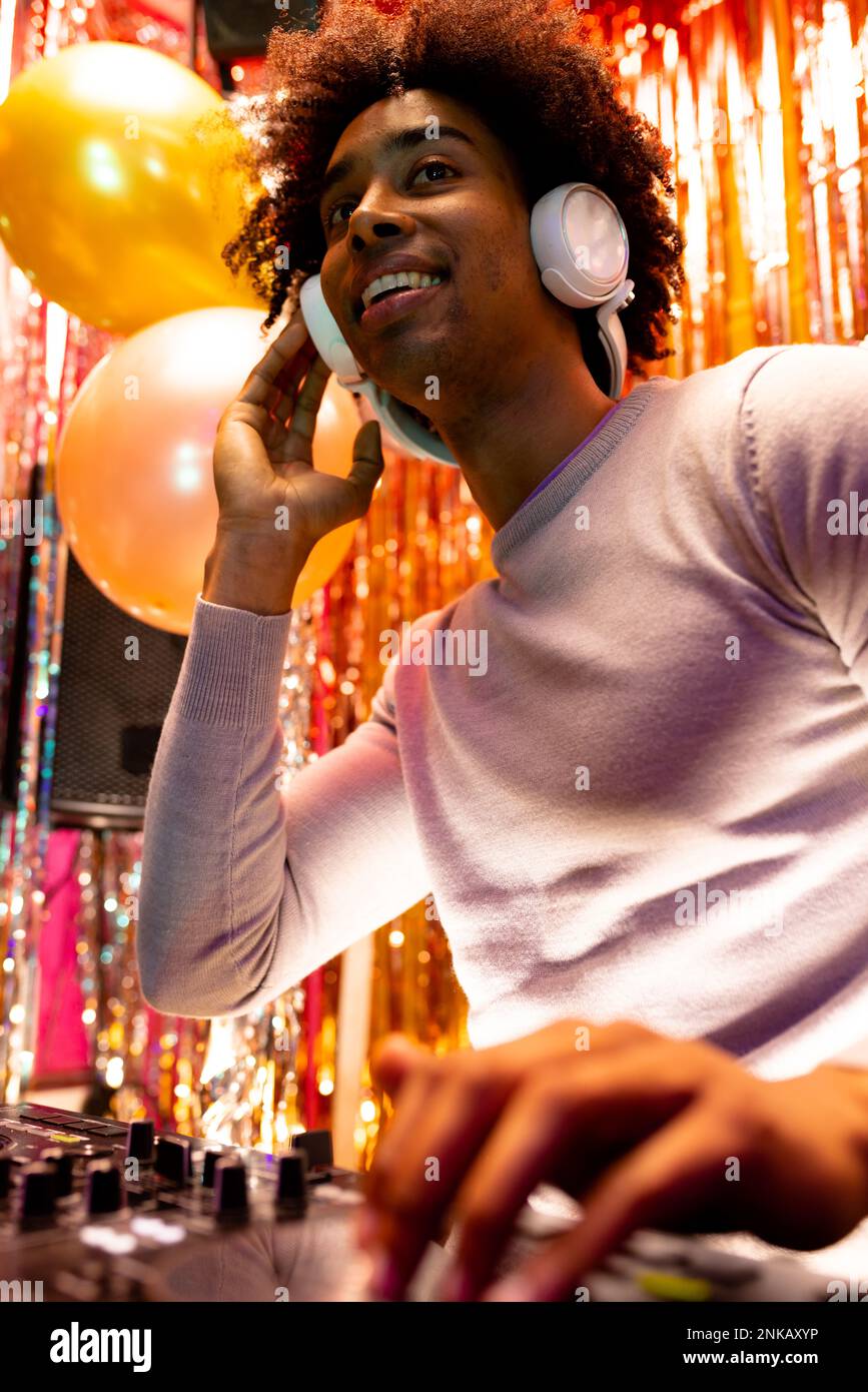 Vertikales Bild eines lächelnden afroamerikanischen djs in Kopfhörern, der in einem Nachtclub Musik spielt Stockfoto