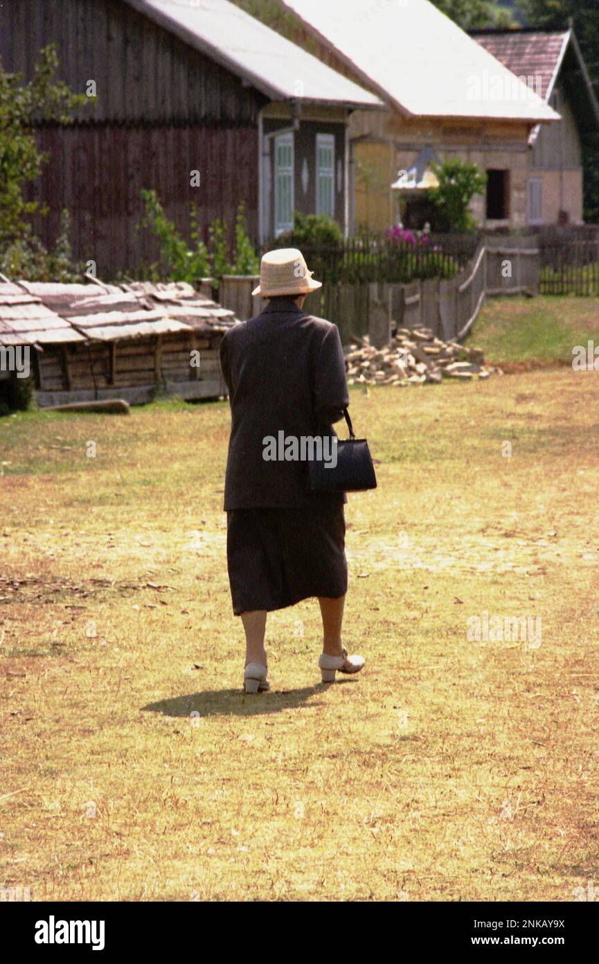 Suceava County, Rumänien, 1998. Ältere Frau in eleganter Kleidung, die durch das Dorf spaziert. Stockfoto