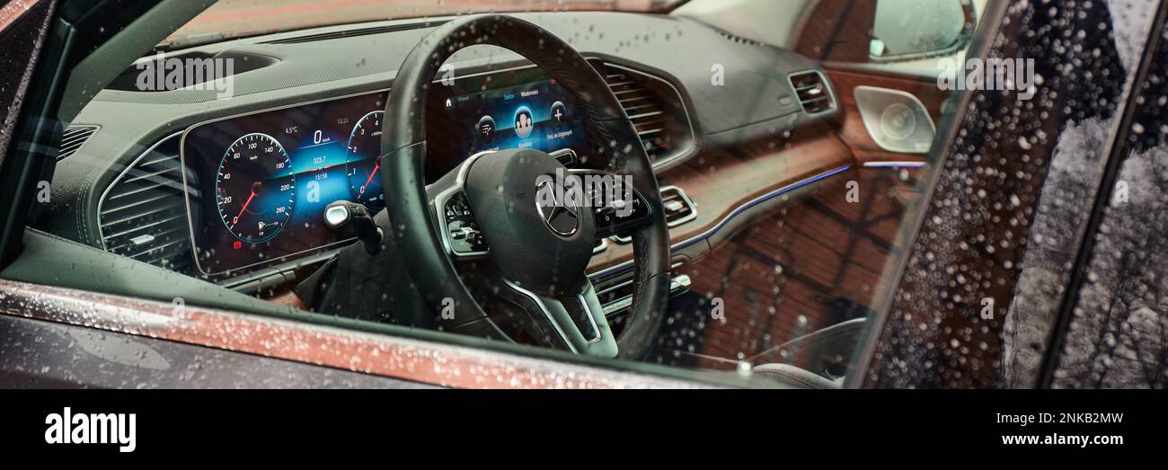 Die Hütte des luxuriösen Mercedes GLE ist mit echtem Holz und Leder und einem riesigen Multimedia-Bildschirm MBUX ausgestattet. Blick durch das Glas mit Regentropfen. Ruda Slaska, Stockfoto