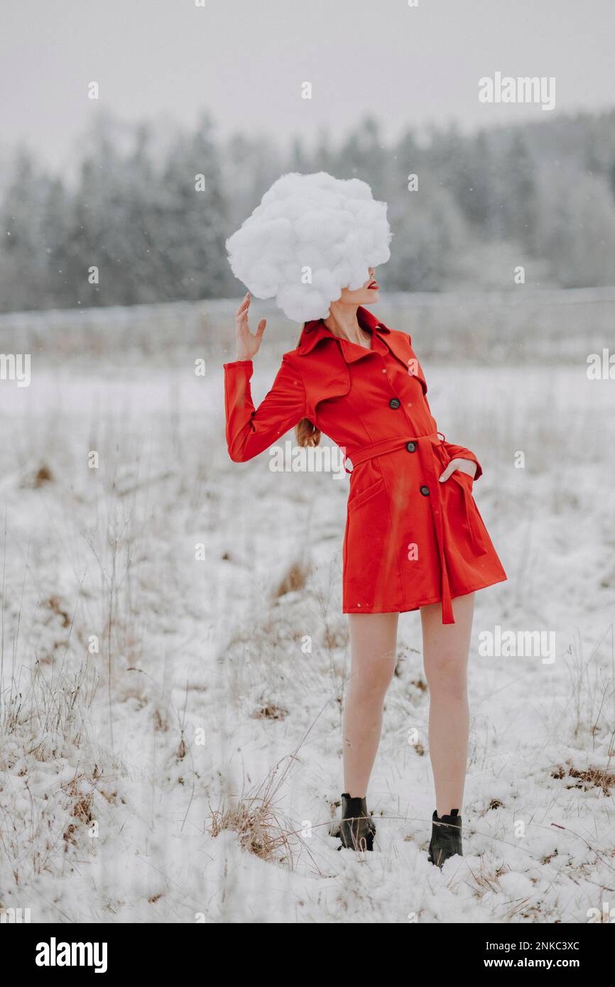 Frau in rotem Mantel mit Wolken auf dem Kopf im Schnee Stockfoto