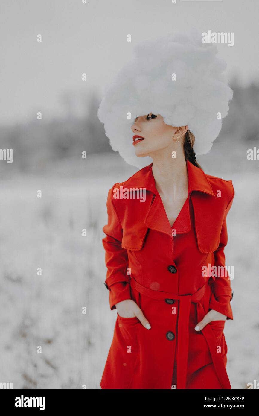 Frau in rotem Mantel mit Wolken auf dem Kopf im Schnee Stockfoto
