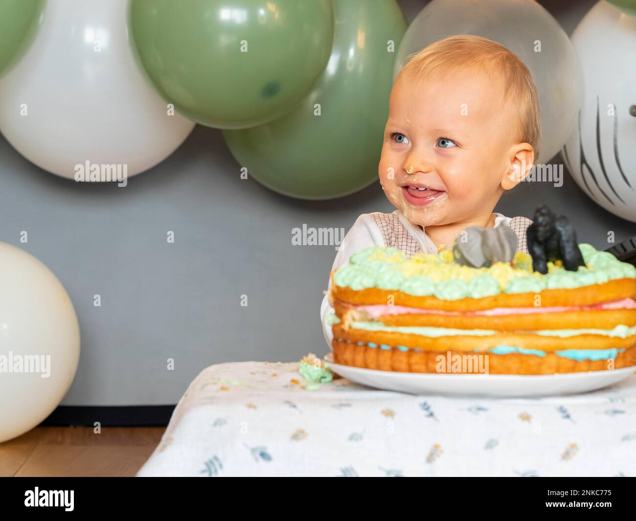 Ein einjähriger Junge sitzt an seinem ersten Geburtstag vor seinem Geburtstagskuchen und versucht zu sehen, ob er gut schmeckt Stockfoto