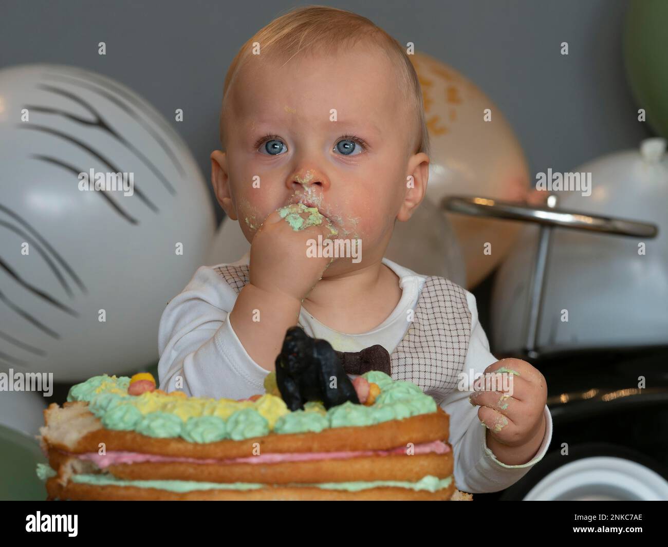 Ein einjähriger Junge sitzt an seinem ersten Geburtstag vor seinem Geburtstagskuchen und versucht zu sehen, ob er gut schmeckt Stockfoto