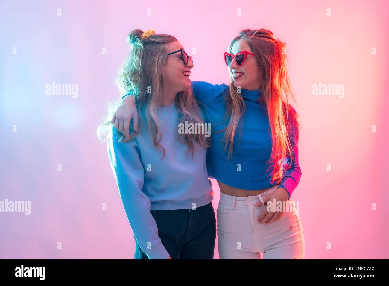 Zwei junge blonde weiße Frauen, die in der Disco tanzen, lächelnd und umarmt porträtieren Stockfoto