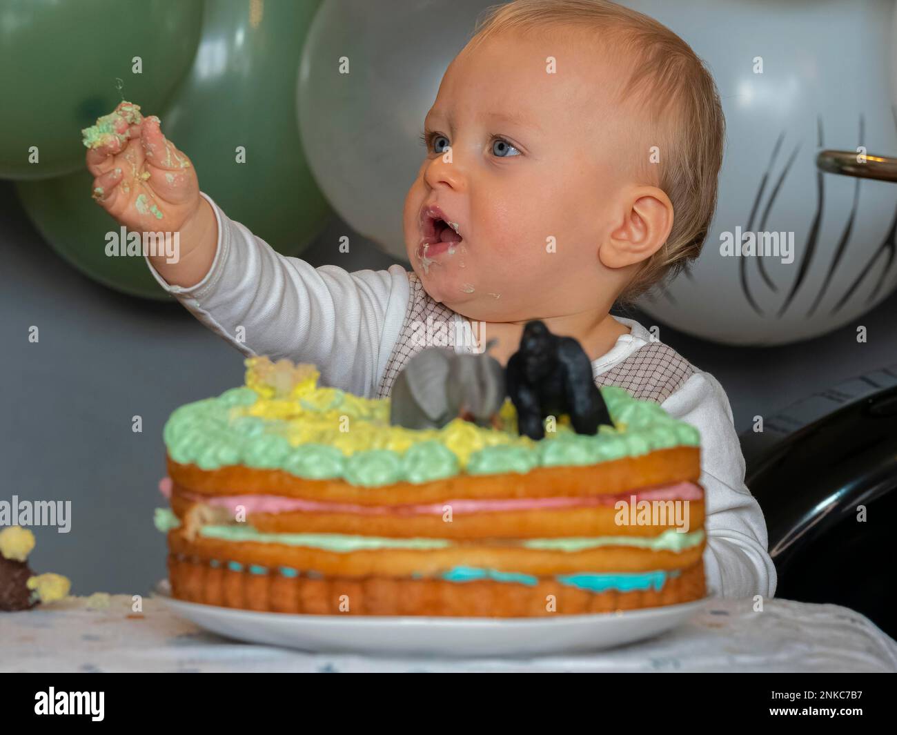 Ein einjähriger Junge sitzt an seinem ersten Geburtstag vor seinem Geburtstagskuchen und versucht zu sehen, ob er gut schmeckt Stockfoto