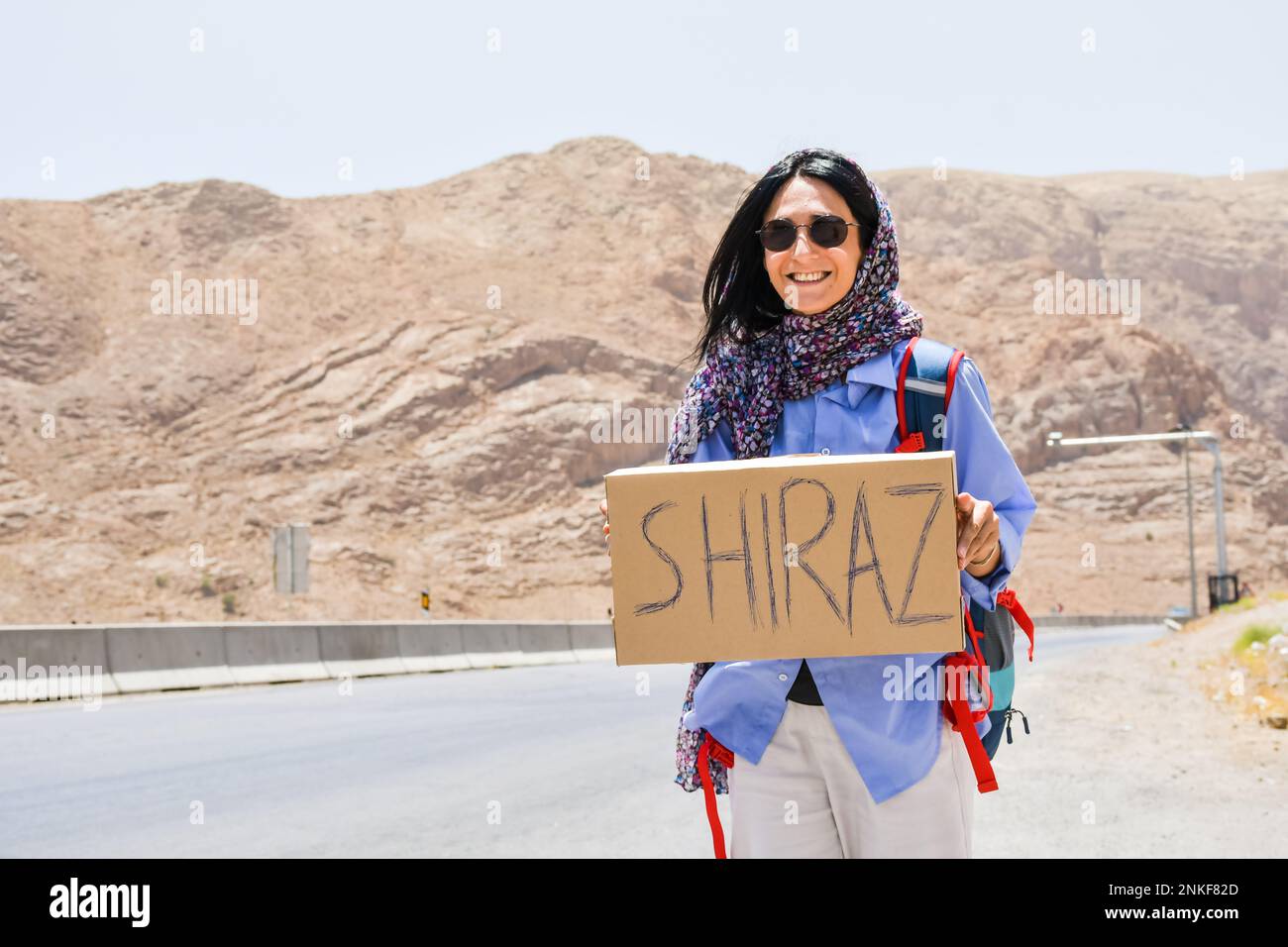 Junge Reisende Frau steht auf einer Tramptour mit einem Schild nach Shiraz und Daumen hoch mit Lächeln im Iran. Solo Safe Travel in Asia Concept Stockfoto