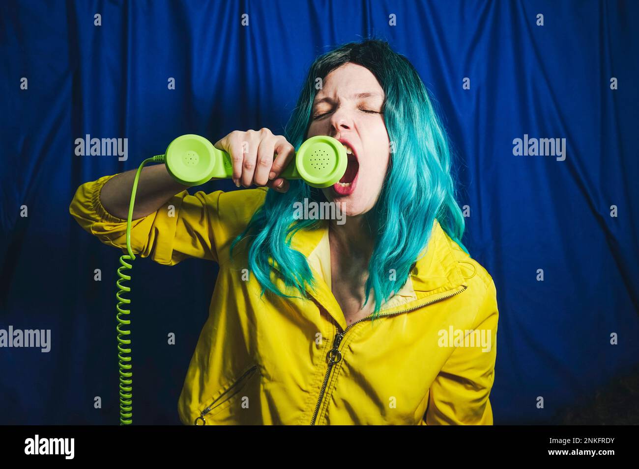 Frau schreit mit Telefonhörer als Lautsprecher vor blauem Hintergrund Stockfoto