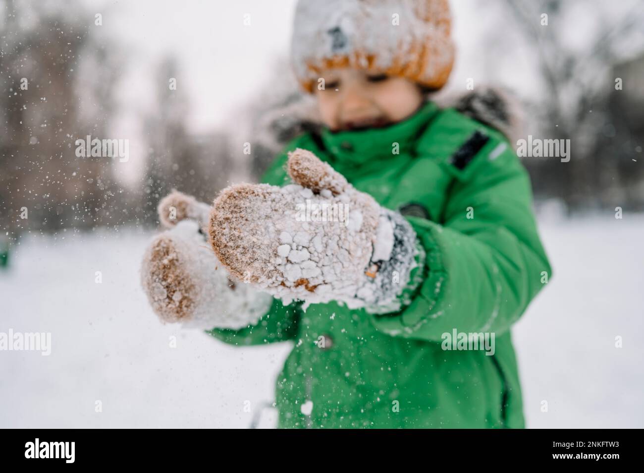 Ein Junge mit Handschuhen, der mit Schnee spielt Stockfoto