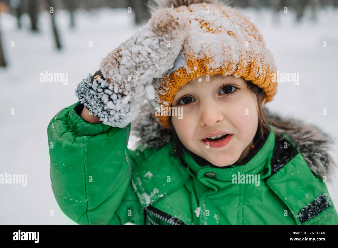 Ein unschuldiger Junge, der eine Strickmütze und Handschuhe trägt, die mit Schnee bedeckt sind Stockfoto