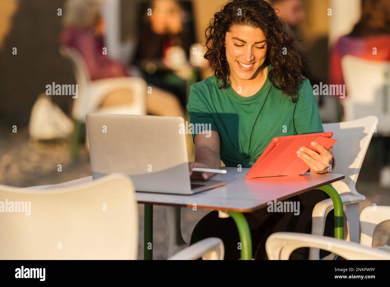 Glückliche Frau mit Tablet-PC, die bei Sonnenuntergang in einem Café im Freien sitzt Stockfoto