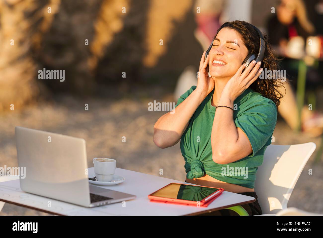 Glückliche Frau mit kabellosen Kopfhörern, die im Café im Freien Musik hört Stockfoto
