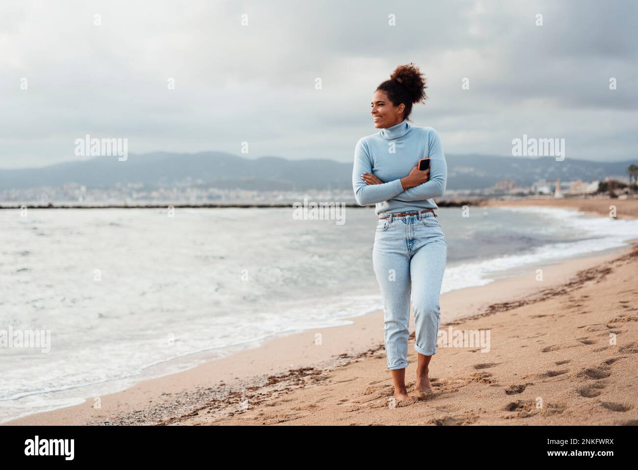 Glückliche Frau mit verschränkten Armen, die am Strand stand Stockfoto