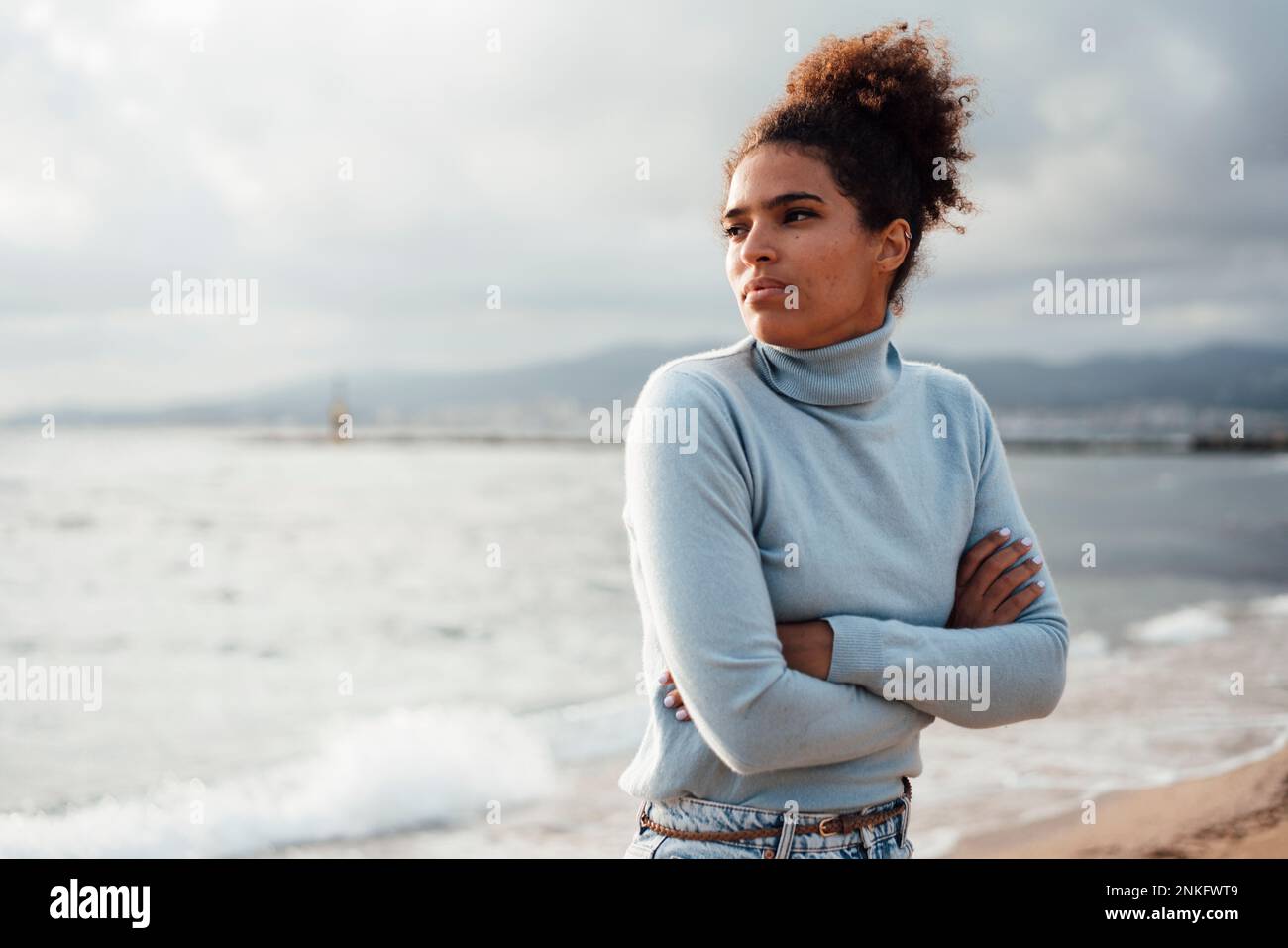 Rücksichtsvolle junge Frau mit gekreuzten Armen am Strand Stockfoto