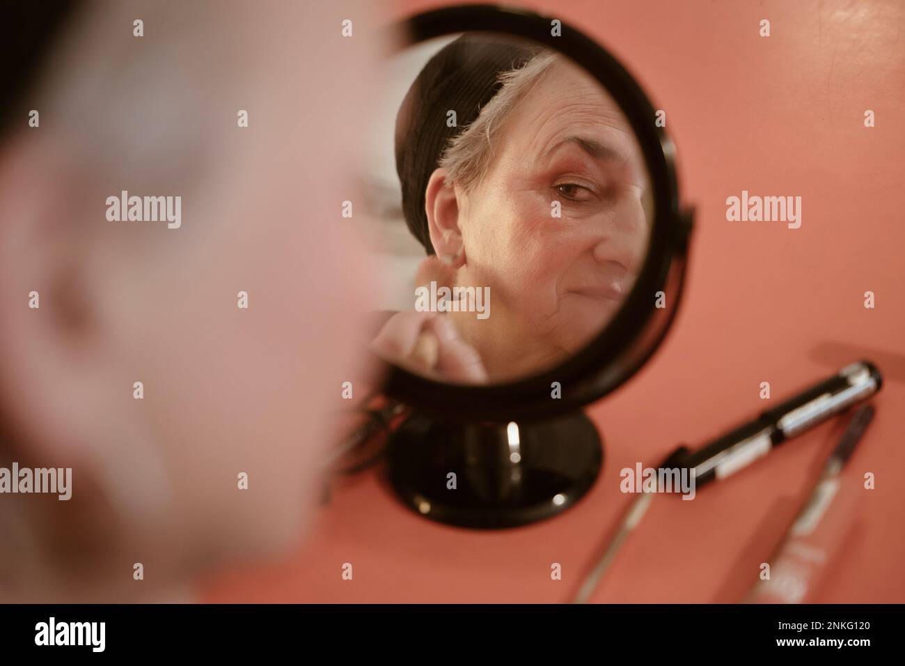 Seniorin, die zu Hause in den Spiegel schaut und sich schminkt Stockfoto