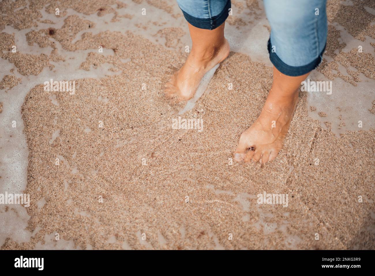 Frau steht auf nassem Sand am Strand Stockfoto