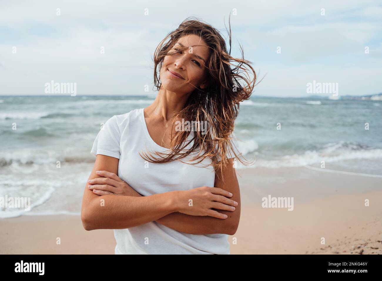 Lächelnde Frau mit gekreuzten Armen am Strand Stockfoto