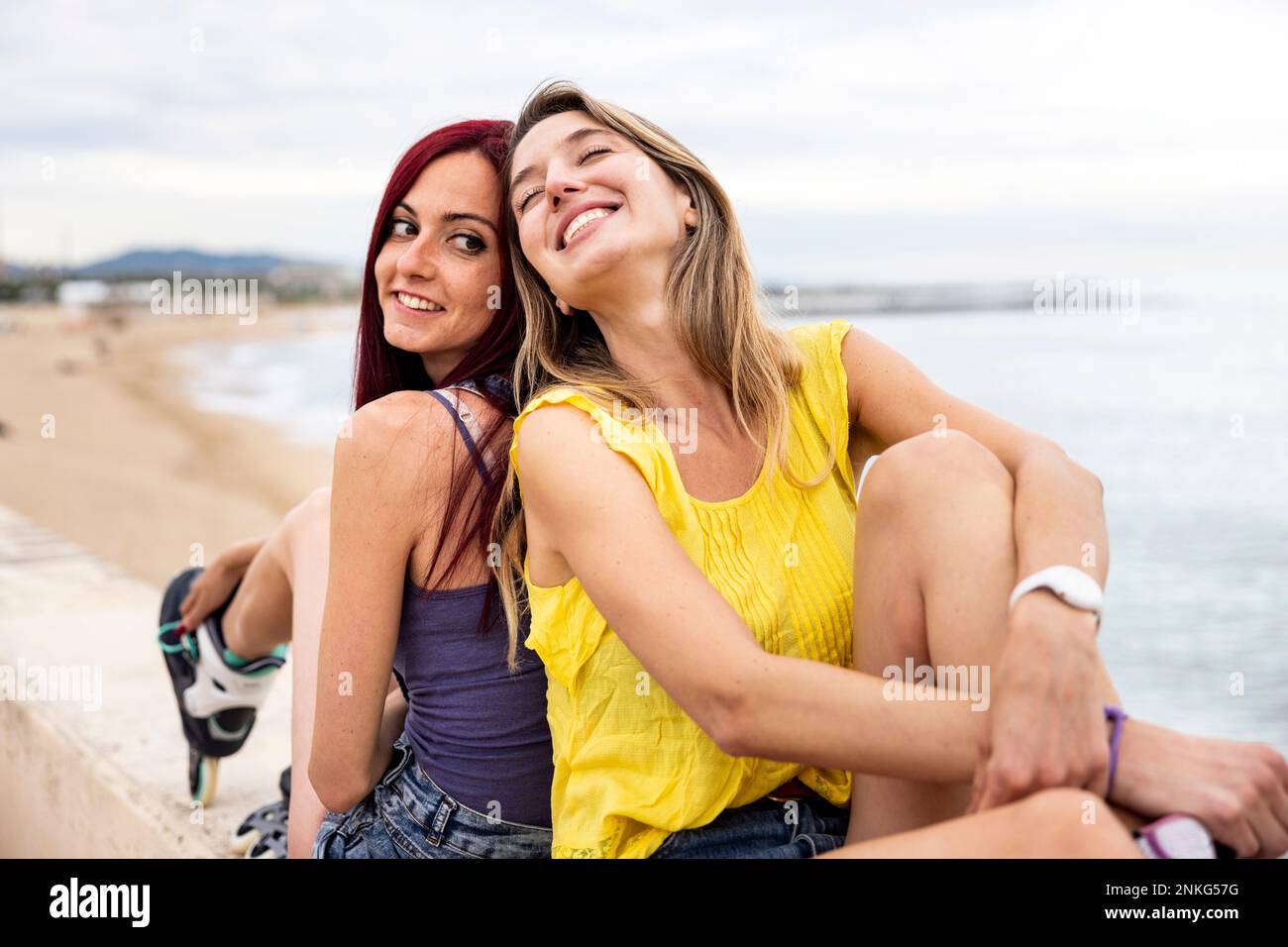 Fröhliche Freunde, die sich Rücken an Rücken an der Promenade auf dem Meer lehnen Stockfoto