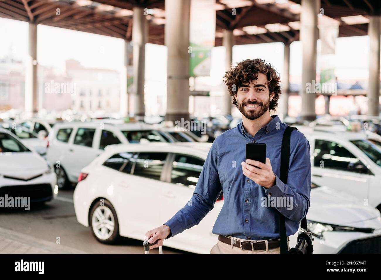 Glücklicher Geschäftsmann mit Smartphone vor Autos Stockfoto