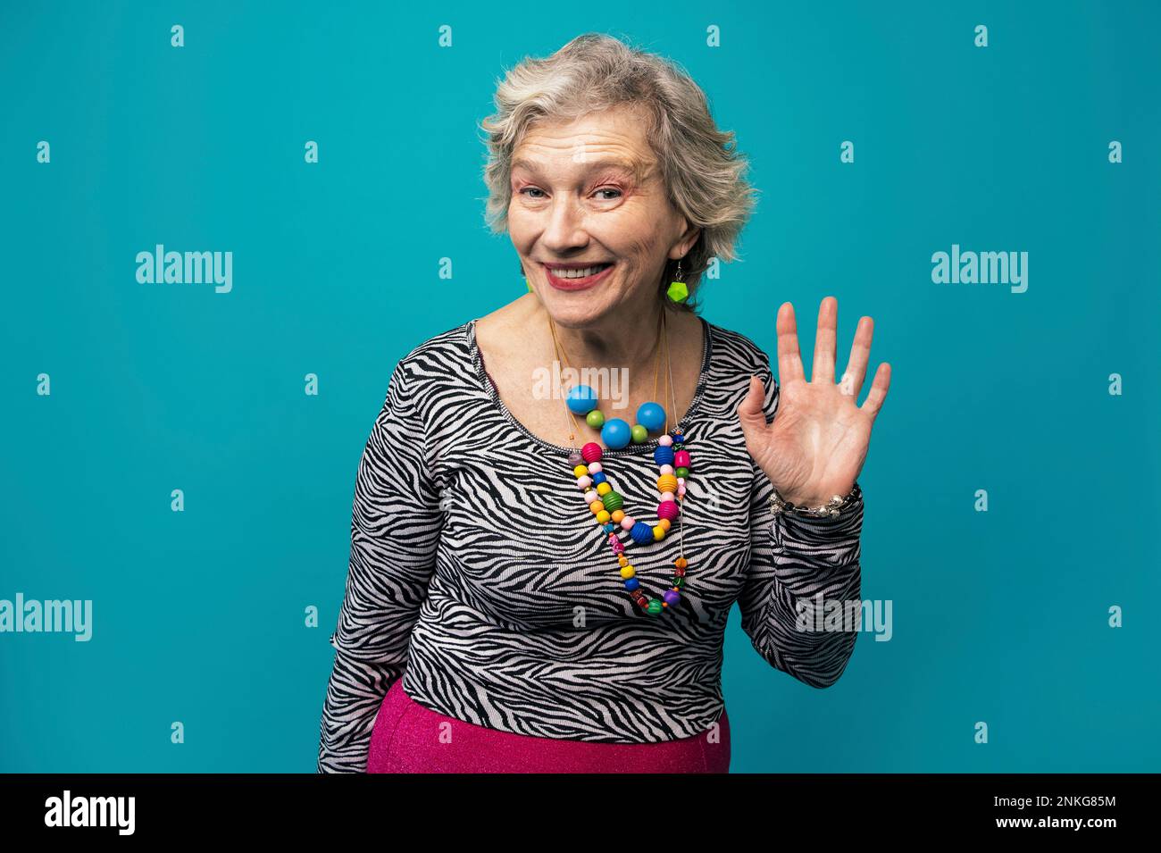 Glückliche ältere Frau, die vor türkisfarbenem Hintergrund winkt Stockfoto