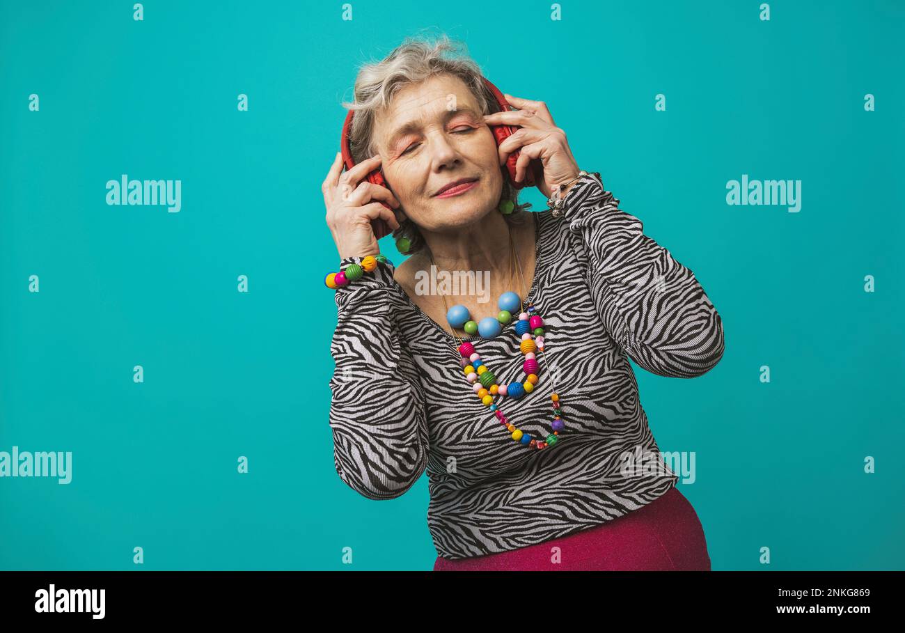 Seniorin mit Kopfhörern, die Musik vor farbigem Hintergrund hört Stockfoto