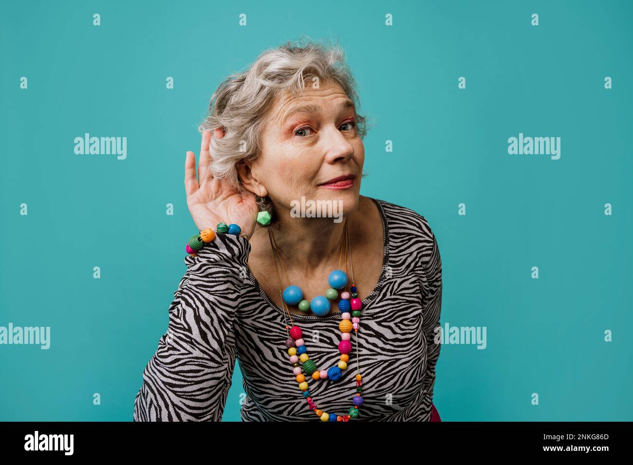 Frau, die das Ohr umschubst, um vor türkisfarbenem Hintergrund zu hören Stockfoto