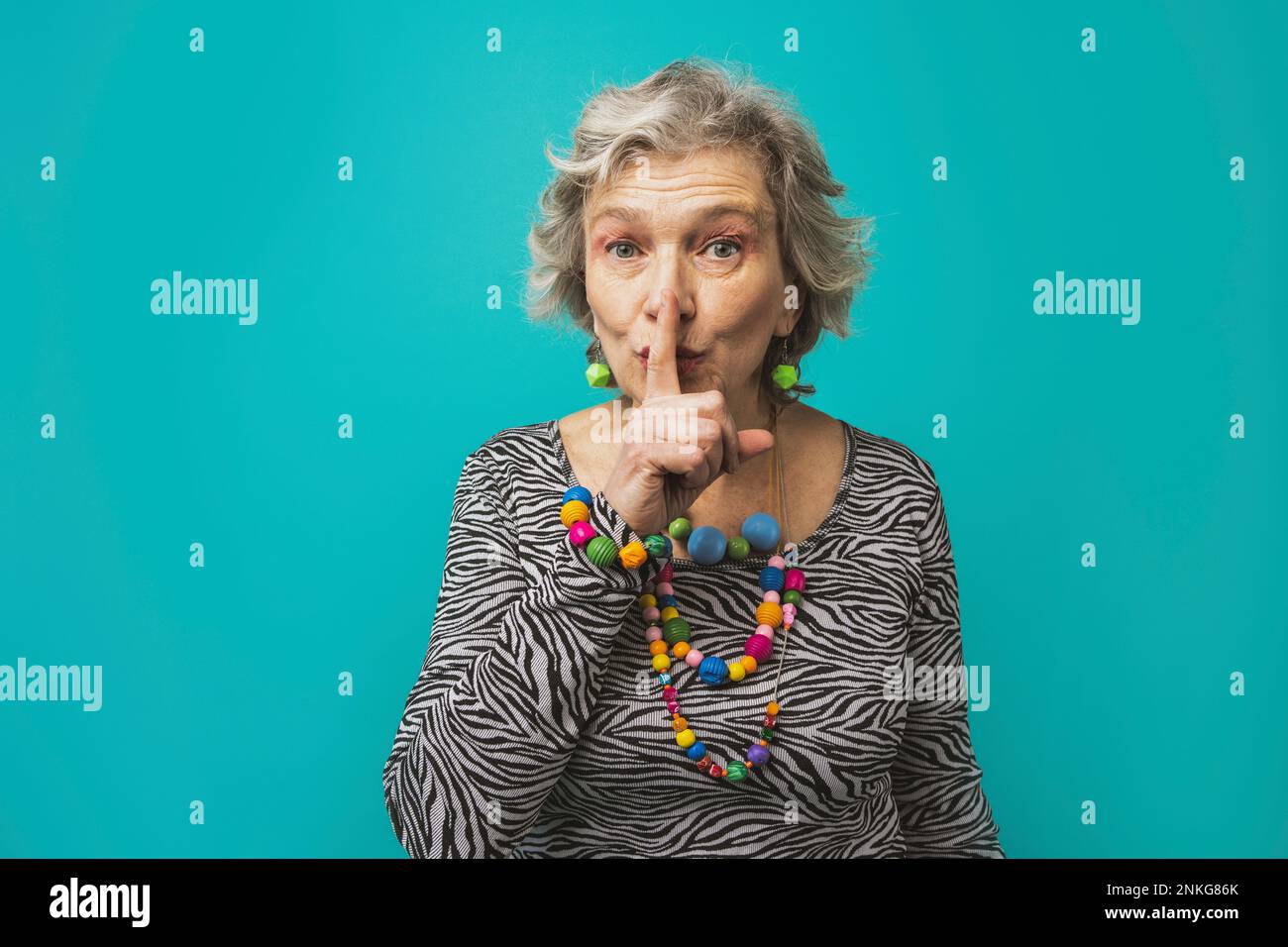 Ältere Frau mit Finger auf den Lippen, die vor einem farbigen Hintergrund steht Stockfoto