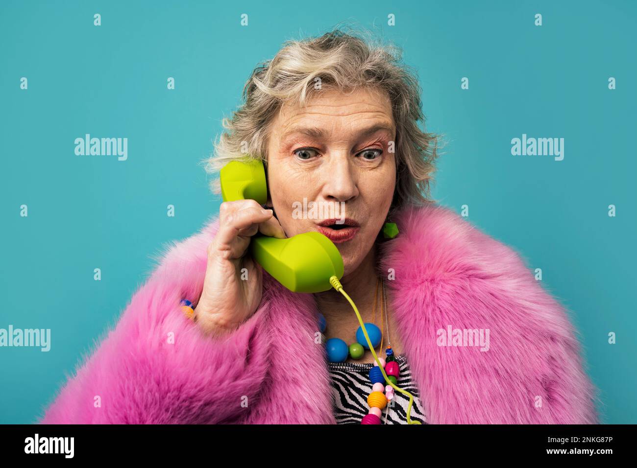 Seniorin, die vor türkisfarbenem Hintergrund telefoniert Stockfoto