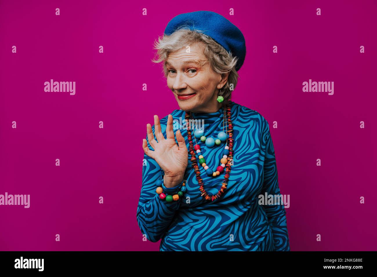 Lächelnde ältere Frau, winkend vor pinkfarbenem Hintergrund Stockfoto