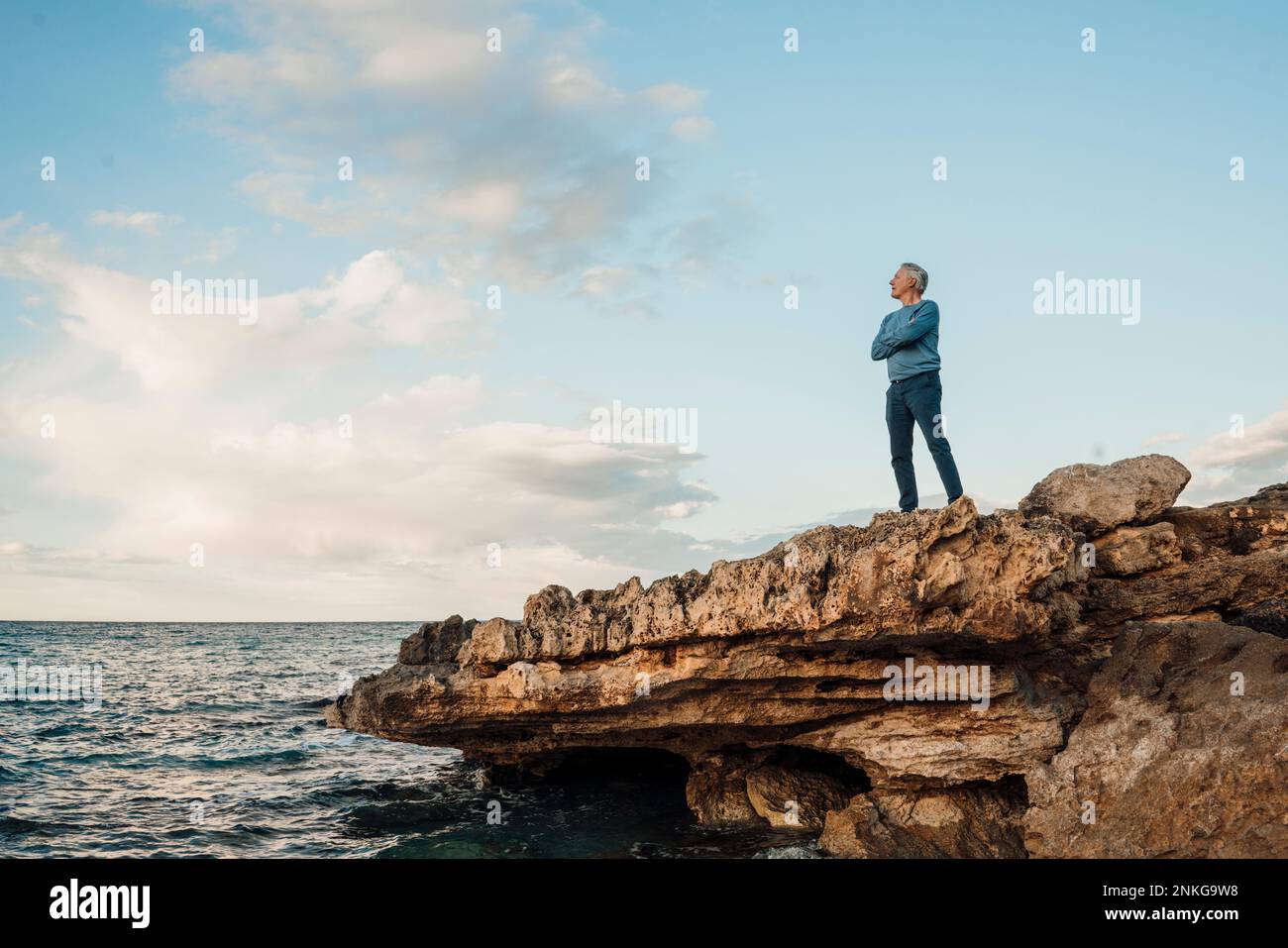 Ein älterer Mann, der mit gekreuzten Armen auf einem Felsen steht Stockfoto