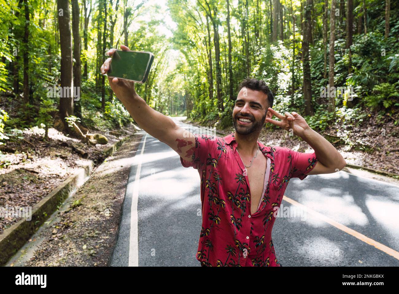 Ein glücklicher Mann zeigt Friedenszeichen und macht Selfie vor Bäumen Stockfoto