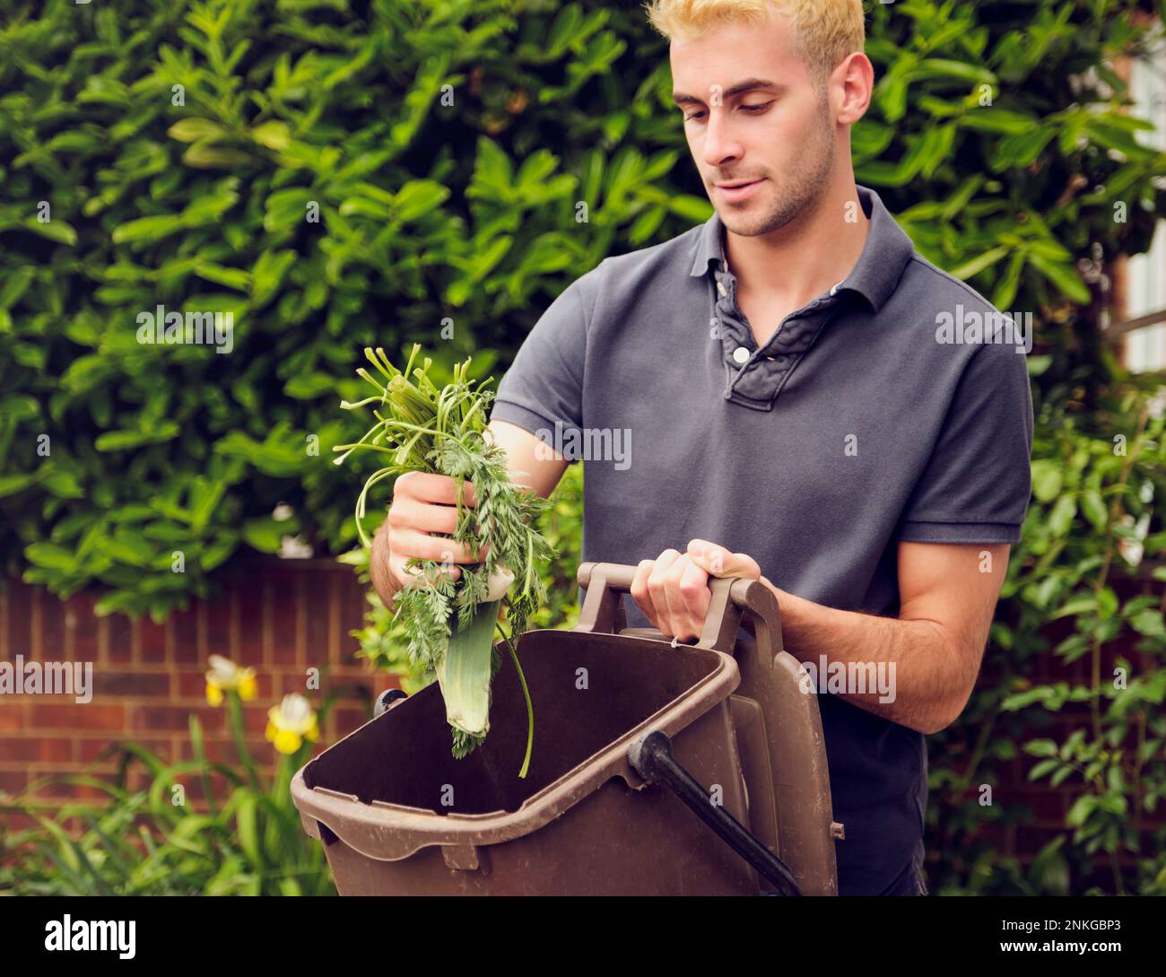Junger Mann, der Lebensmittelabfälle im Garten recycelt Stockfoto