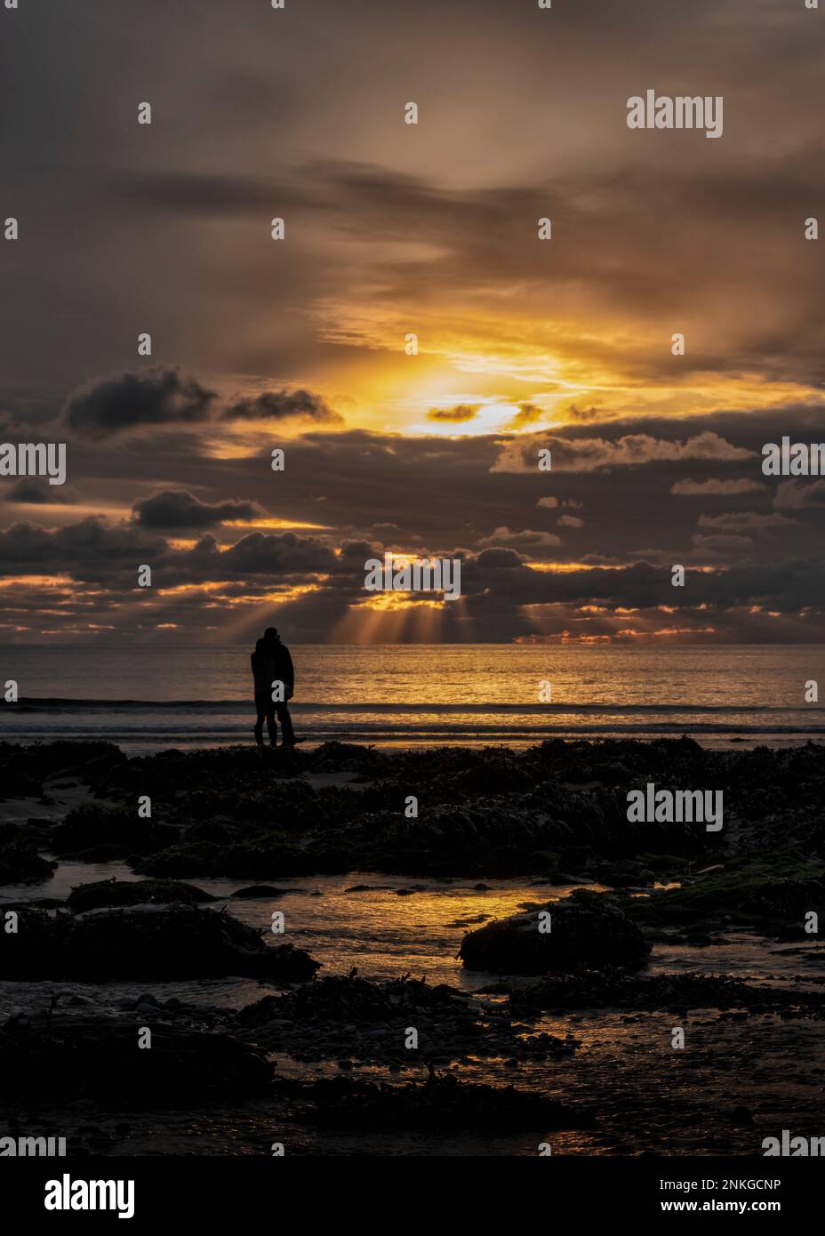 Silhouettenpaar mit Blick auf die Küste am Sunset Beach, Pembrokeshire, Wales Stockfoto