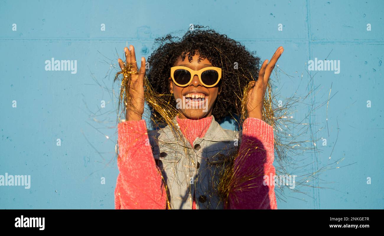 Fröhliche Frau hält goldene Partystrampel vor der blauen Wand Stockfoto