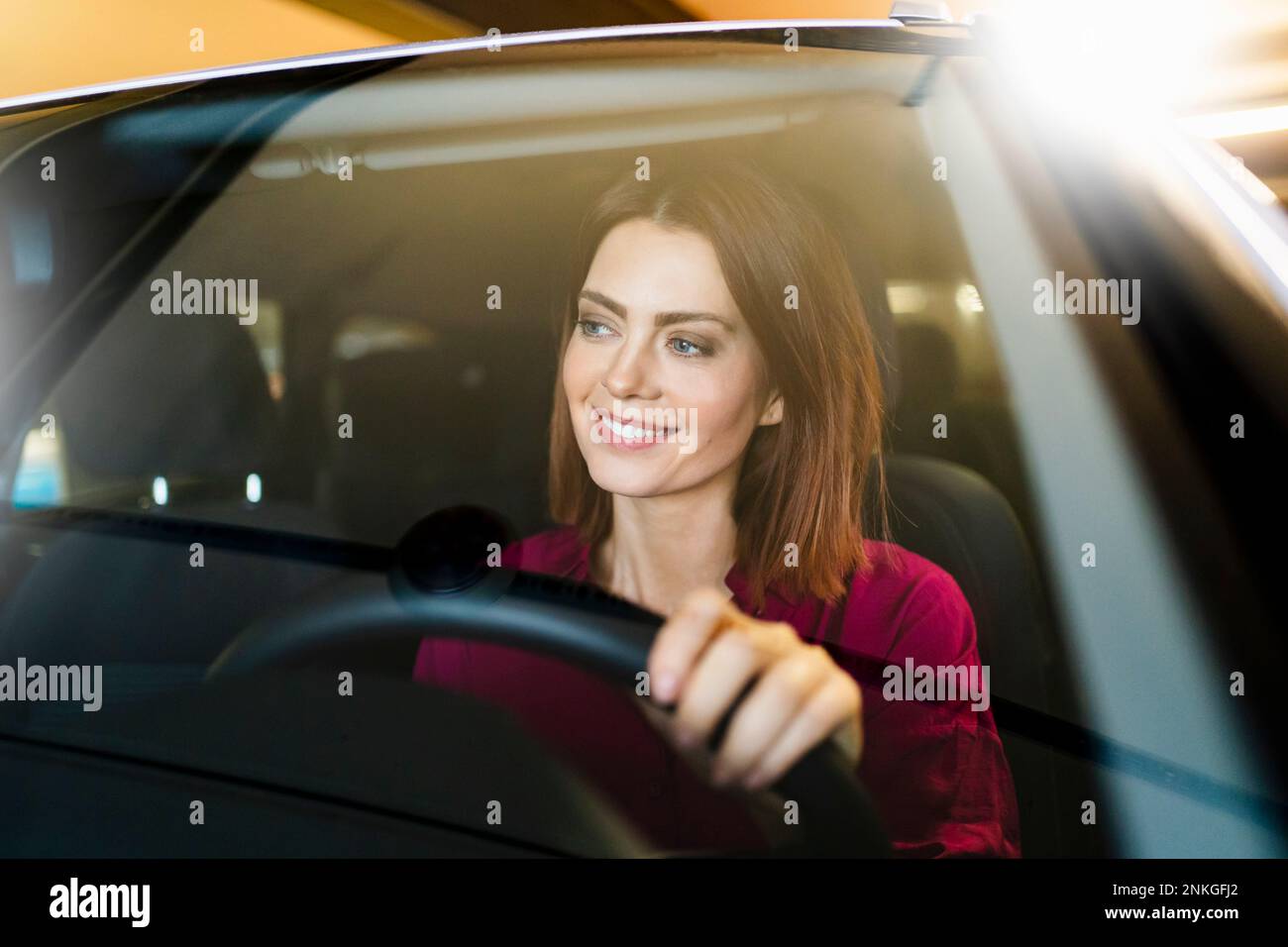 Glückliche Geschäftsfrau, die Auto fährt, durch die Windschutzscheibe gesehen Stockfoto
