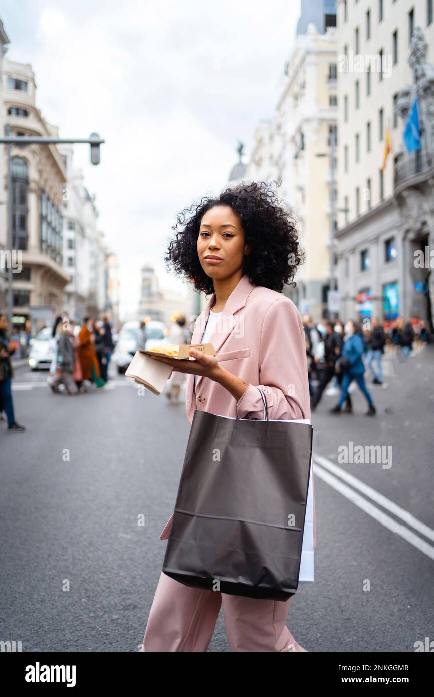 Junge Geschäftsfrau mit Essen und Einkaufstüte, die auf der Straße spaziert Stockfoto