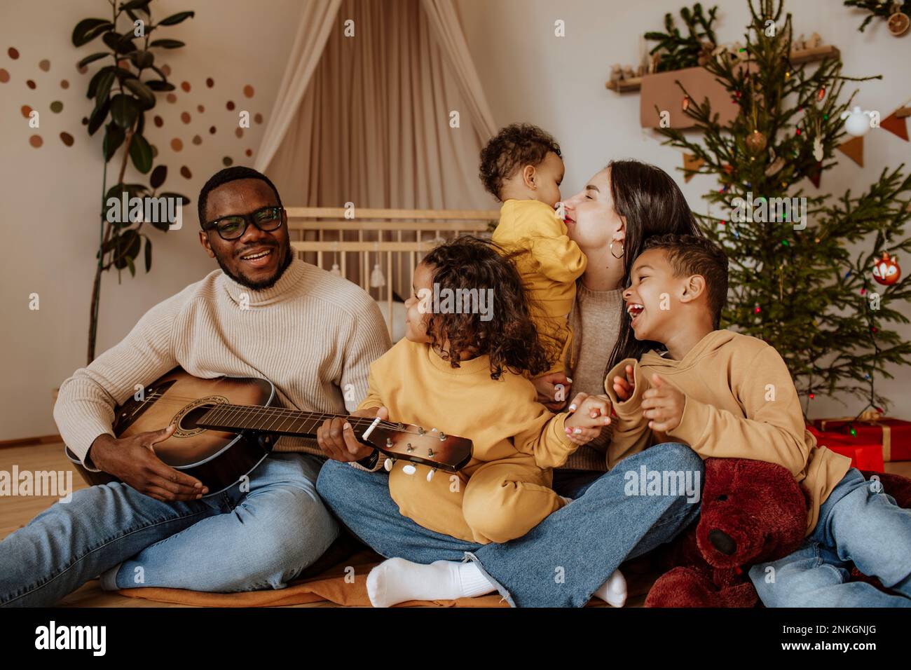 Fröhliche Familie, die zu Weihnachten Zeit mit ihr zusammen verbringt und Gitarre spielt Stockfoto
